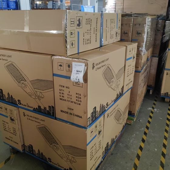 Real shipment image — stacked radar-sensor solar street-light cartons in warehouse storage.