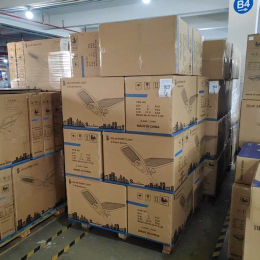 Solar product shipment update showing palletized cartons printed with solar street-light and radar-sensor illustrations in a warehouse aisle