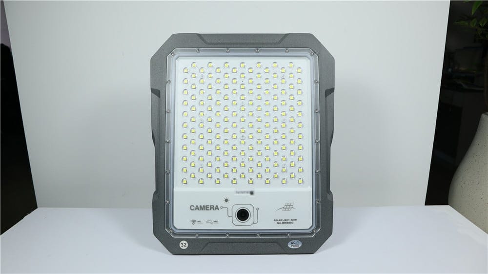 Front of a camera-equipped flood light showing the lens below its LEDs