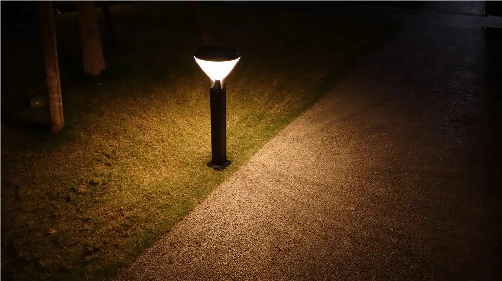 A lit garden bollard beside a path at night