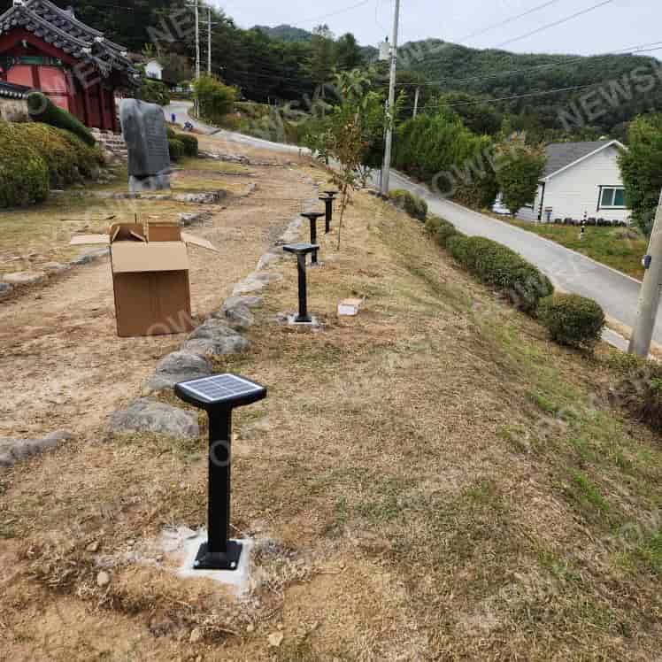 Square-top solar bollard lights mounted along a stone-edged path on sloping ground