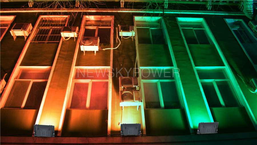 Promotional illustration of coloured floodlights washing a building facade in orange and green.