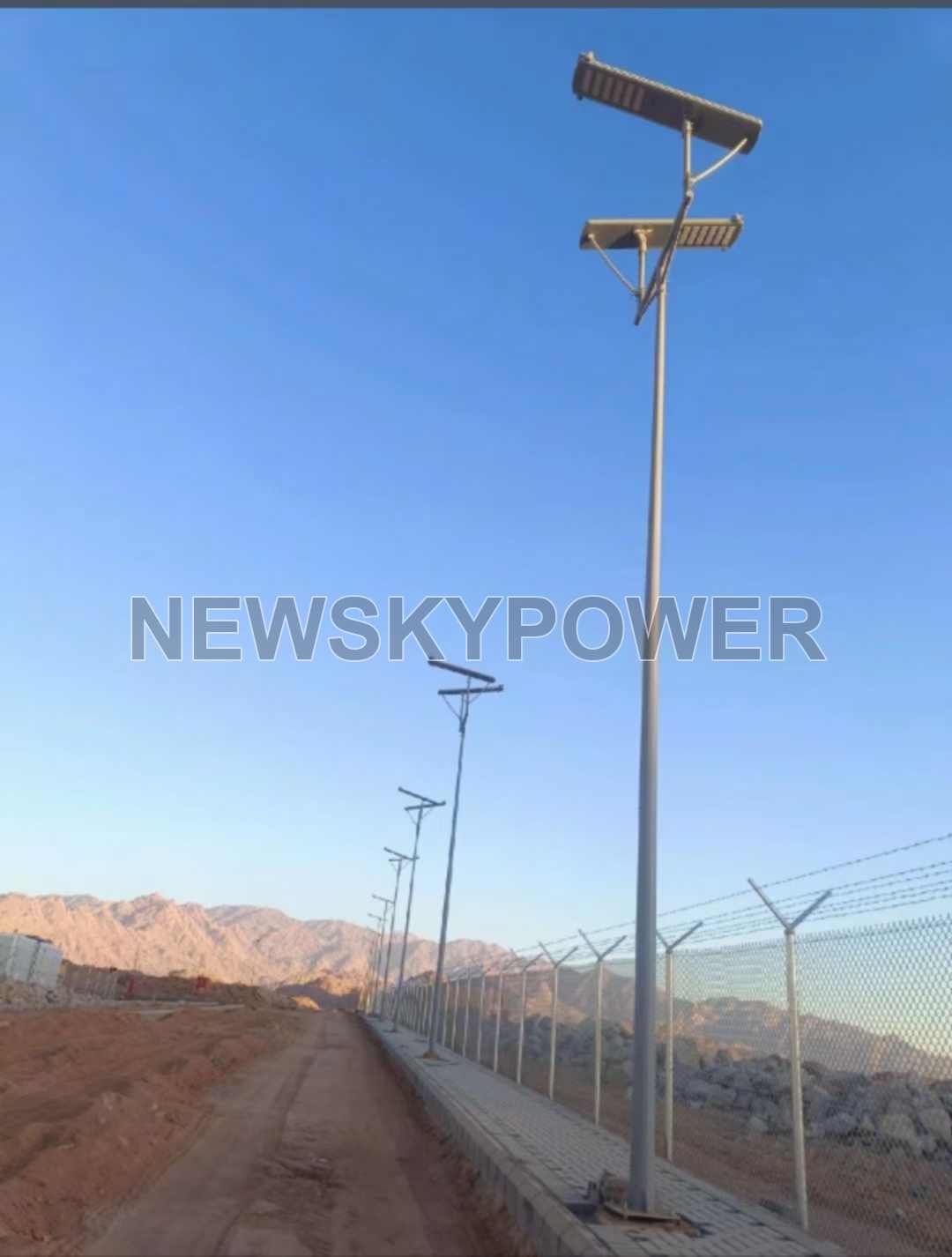 Solar street-light poles beside a fenced road in daylight