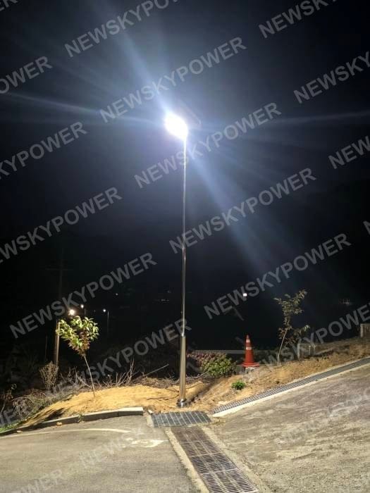 Solar street light beside a sloping paved road and drainage channel at night