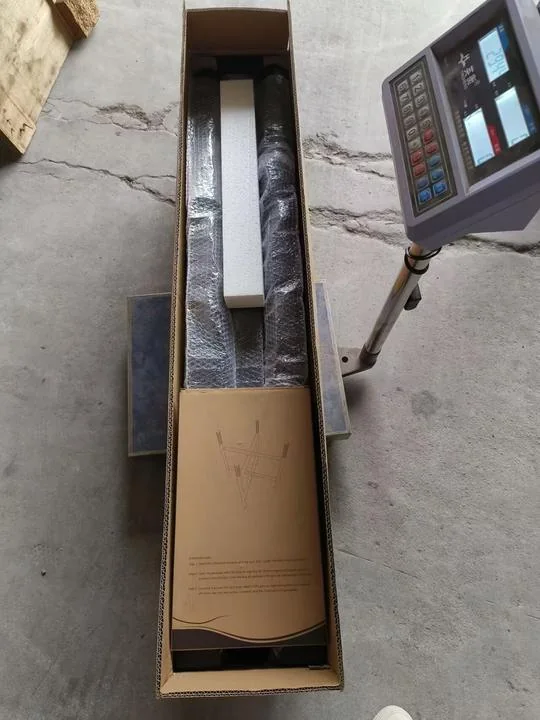 Open carton containing packed pole components beside a weighing-scale display